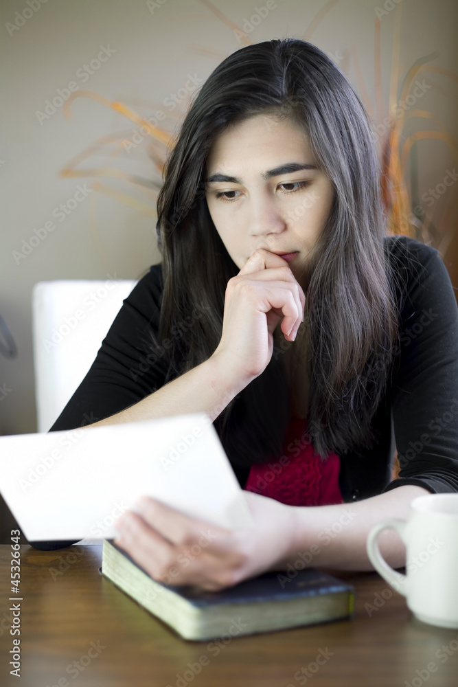Teenage girl or young woman reading a note, worried expression Teenage girl or young woman reading a note, worried expression