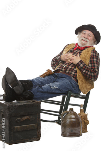 Smiling old cowboy sits in rocking chair with feet up