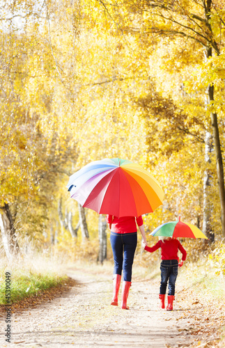 mother with her daughter with umbrellas in autumnal alley