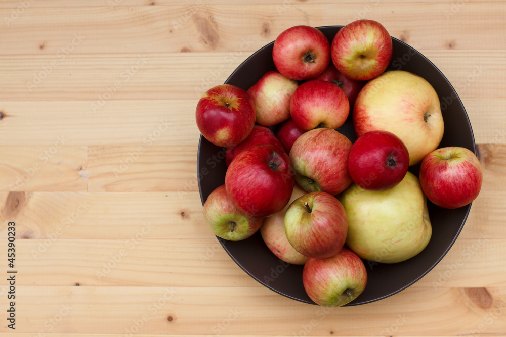 Baby and full size apples in a dish on a pine table Baby and full size apples in a dish on a pine table