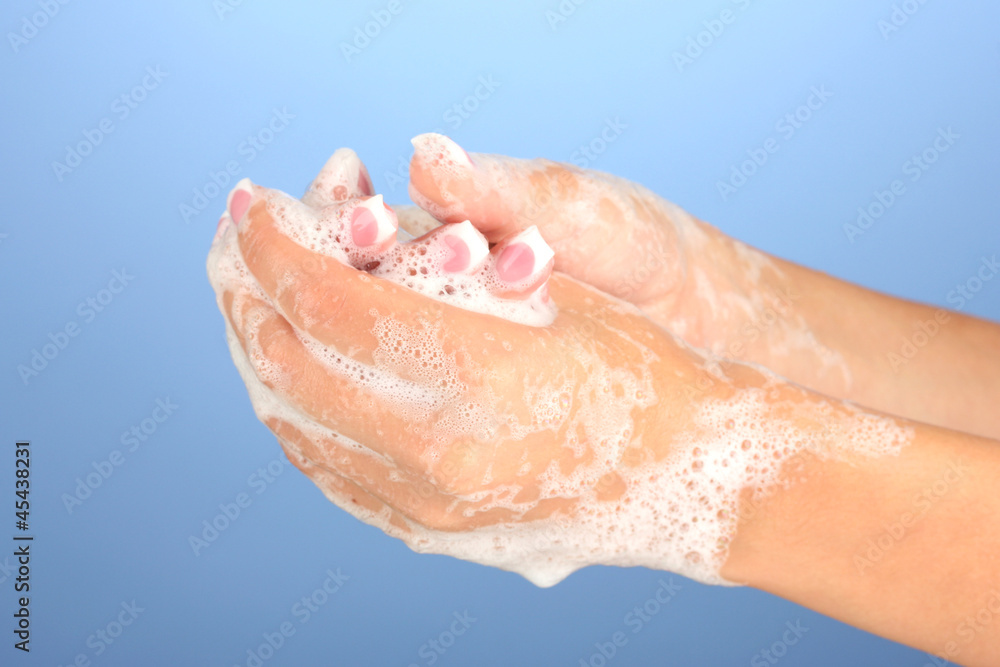 Woman's hands in soapsuds, on blue background close-up Woman's hands in soapsuds, on blue background close-up