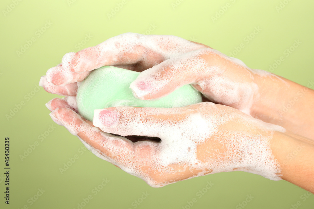 Fototapeta premium Woman's hands in soapsuds, on green background close-up