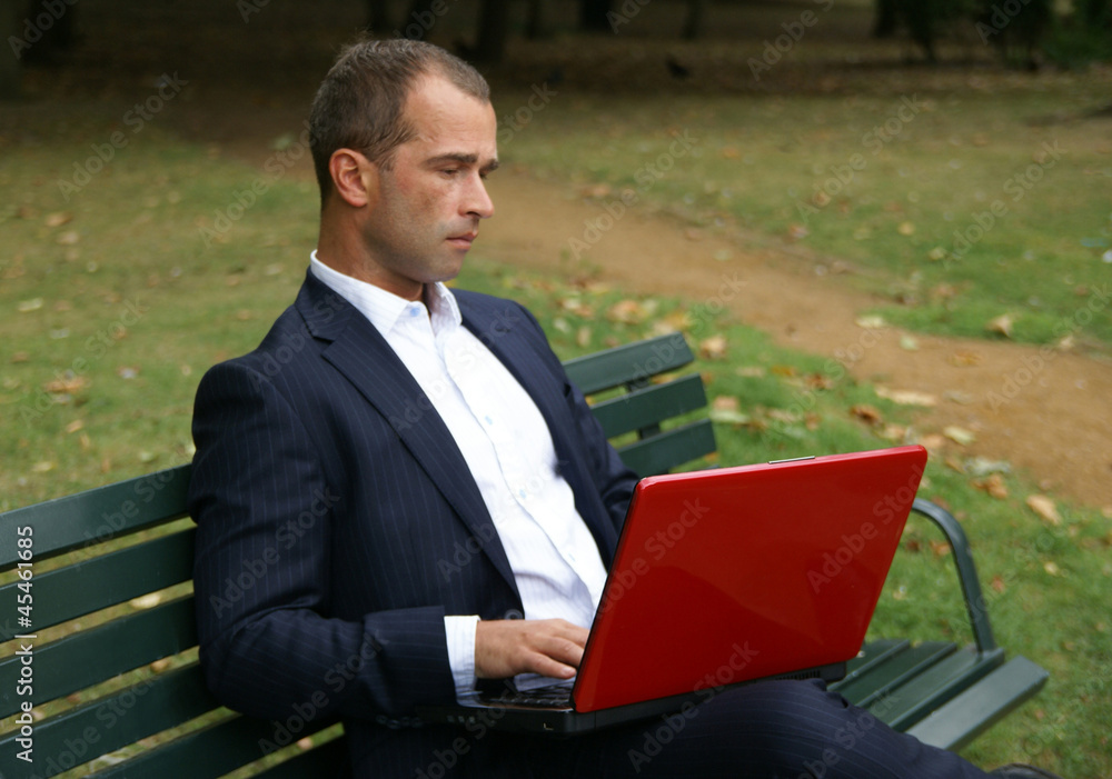 Businessman with a red laptop, sitting on a bench Businessman with a red laptop, sitting on a bench