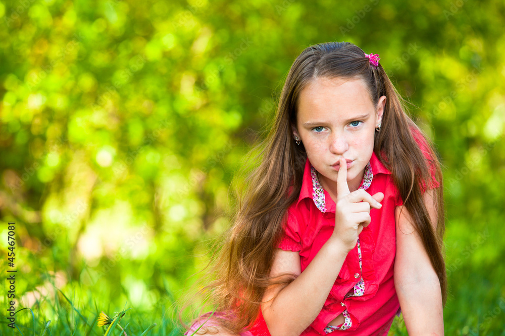 Young girl with her finger over her mouth, hushing.