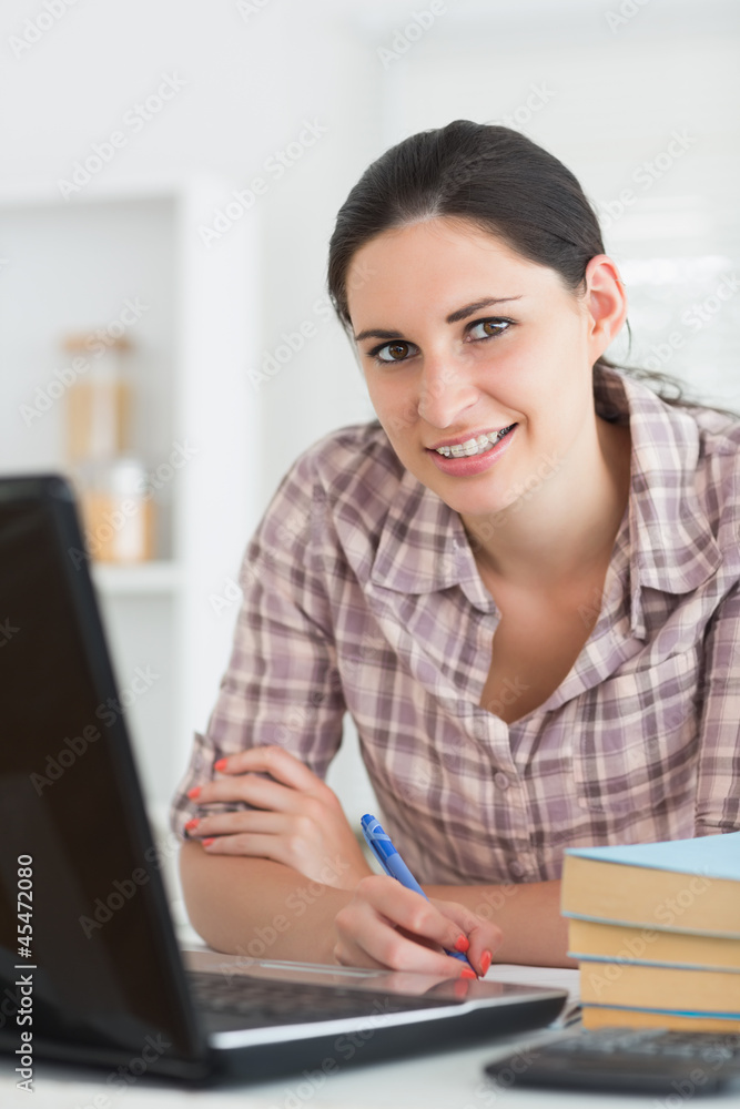Smiling woman writing on notebook beside laptop Smiling woman writing on notebook beside laptop