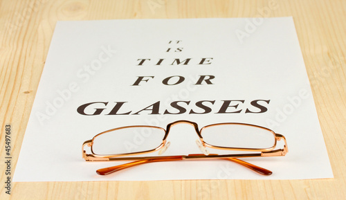 Eyesight test chart with glasses on wooden background close-up