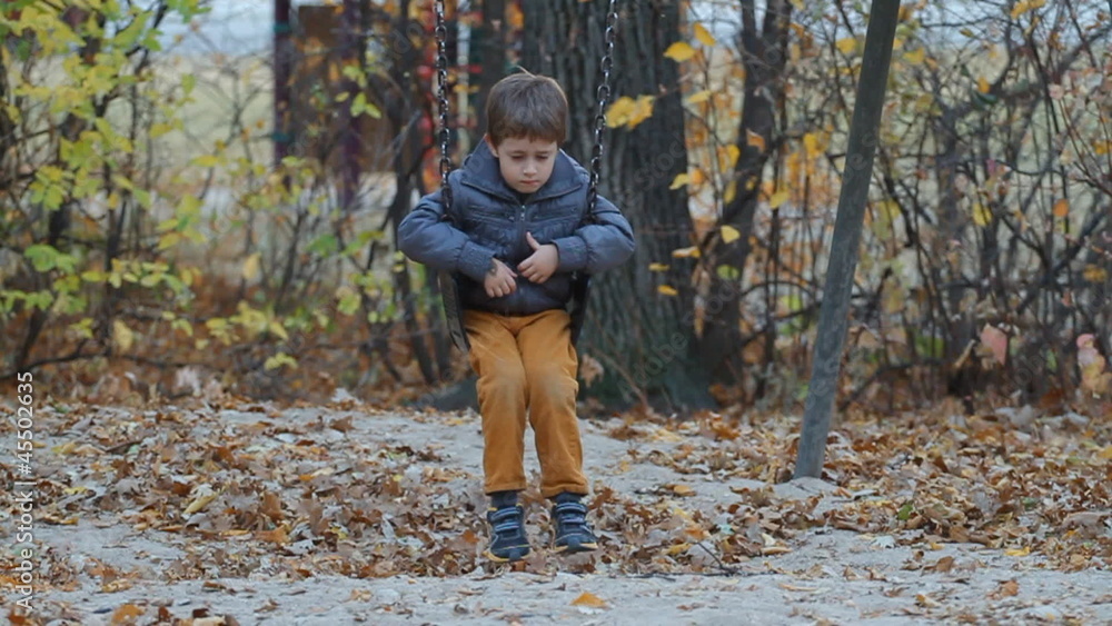 Very sad and cute boy sitting on a swing in a park in autumn Very sad and cute boy sitting on a swing in a park in autumn