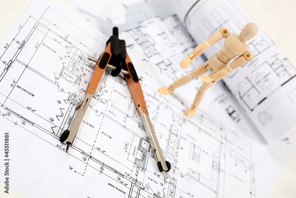 Man standing on building plans looking at measuring instrument Man standing on building plans looking at measuring instrument