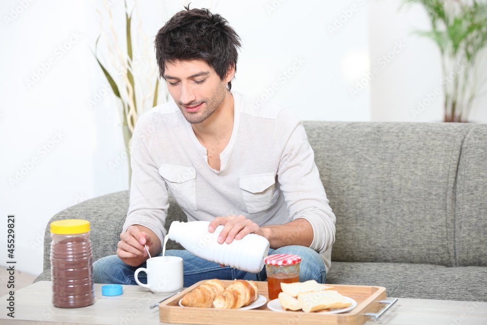 Young man having breakfast in his living room Young man having breakfast in his living room