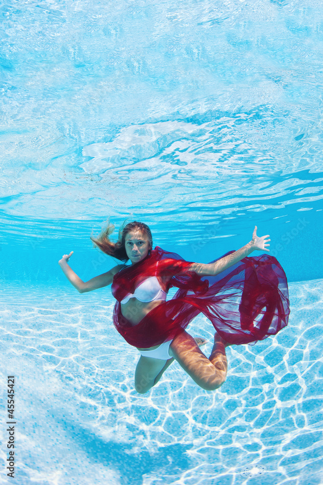 Underwater woman fashion portrait with red veil in swimming pool