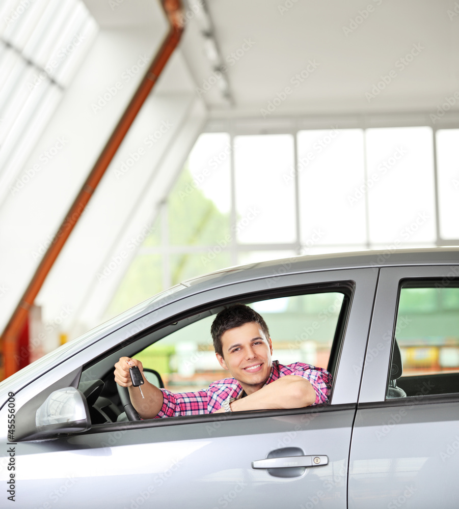 Happy male sitting in his automobile and holding a key