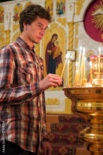 Young man lighting a candle in the church.