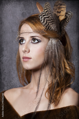 Style redhead girl with feathers on the head. Studio shot.
