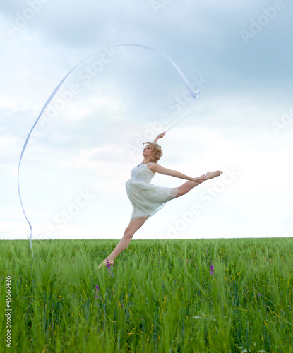Beautiful young woman on a green meadow with a gymnastic ribbon