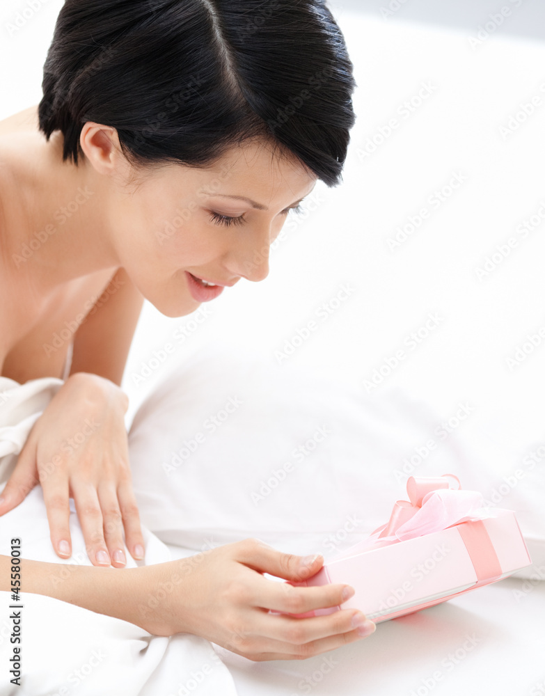 Fototapeta premium Woman finds a present wrapped with pink gift paper in bed