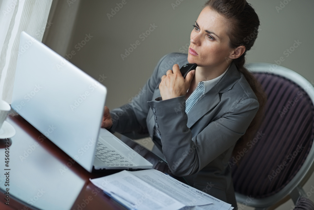 Thoughtful business woman sitting at desk in hotel room Thoughtful business woman sitting at desk in hotel room