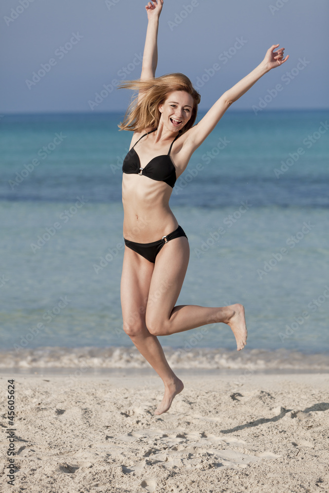 Frau mit Bikini springt fröhlich am Strand Hochformat Frau mit Bikini springt fröhlich am Strand Hochformat