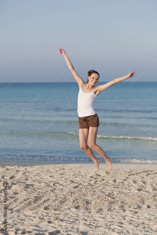 Fröhliche Frau springt lachend am Starnd Hochformat Fröhliche Frau springt lachend am Starnd Hochformat