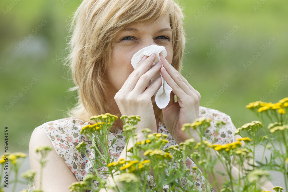 Woman blowing nose into tissue outdoors Woman blowing nose into tissue outdoors