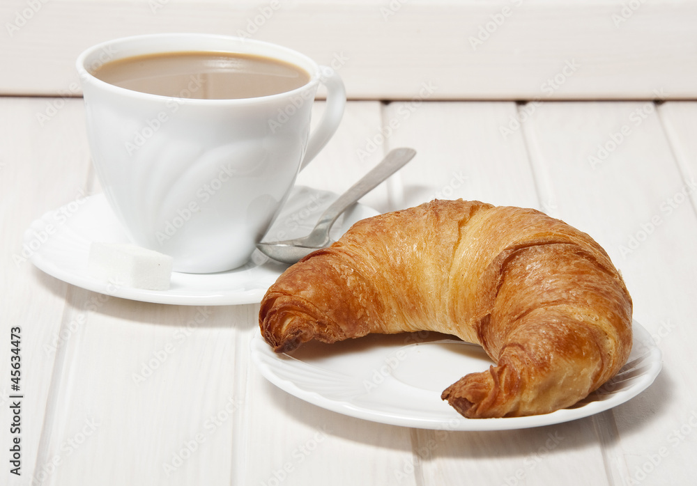 a croissant and a cup of coffeee with milk.
