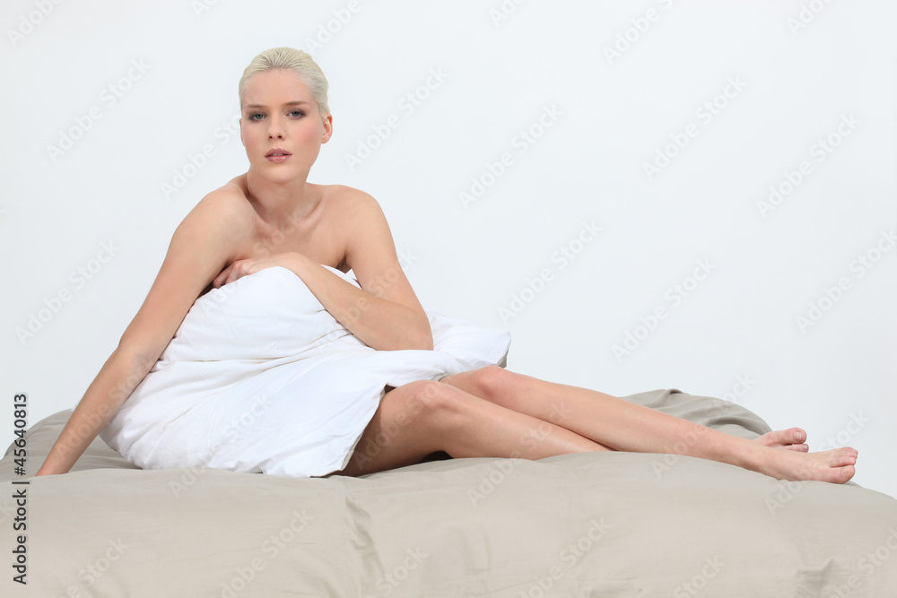 Obraz premium Naked woman sitting on a bed behind a pillow