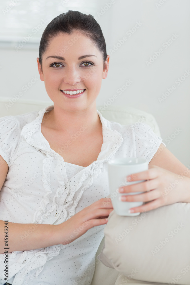 Woman holding a cup sitting on a couch and relaxing Woman holding a cup sitting on a couch and relaxing