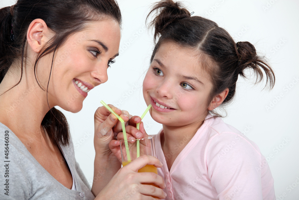 Woman sharing a glass of juice with her little sister Woman sharing a glass of juice with her little sister