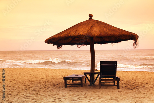 Fototapeta Naklejka Na Ścianę i Meble -  Two empty chairs on beach under umbrella with marine sunset