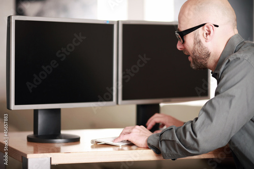 Mann im Büro vor PC Bildschirmen