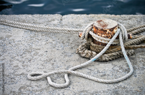Old rusted mooring bollard with knotted nautical ropes