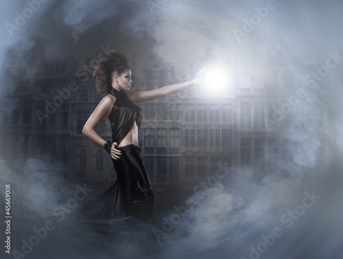 A young brunette witch in a dark dress casting a spell