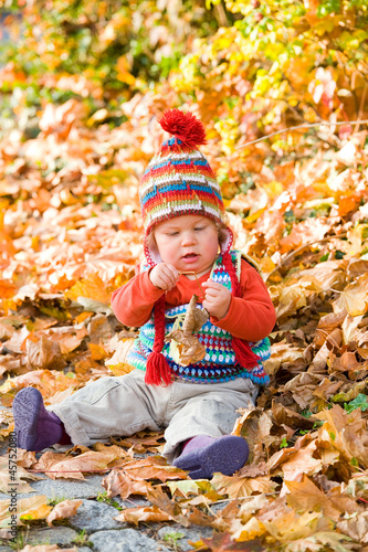 baby is sitting in autumn foliage