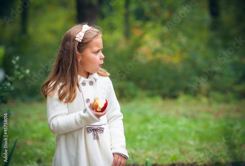 little girl is eating apple outdoor