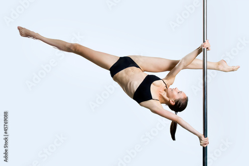 Young sexy woman exercise pole dance against a gray background