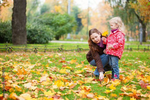 Mother and her little daughter gathering yellow maple leaves in
