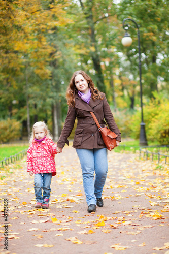Beautiful mother and daughter walking in autumn park together