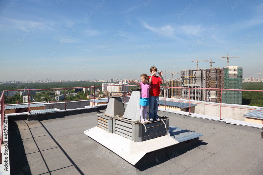 Sister, brother with camera standing on roof of high building