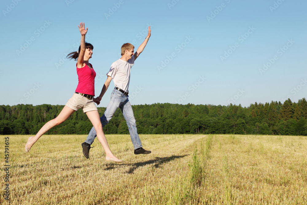 Husband, wife jumping in field near wood, side Husband, wife jumping in field near wood, side
