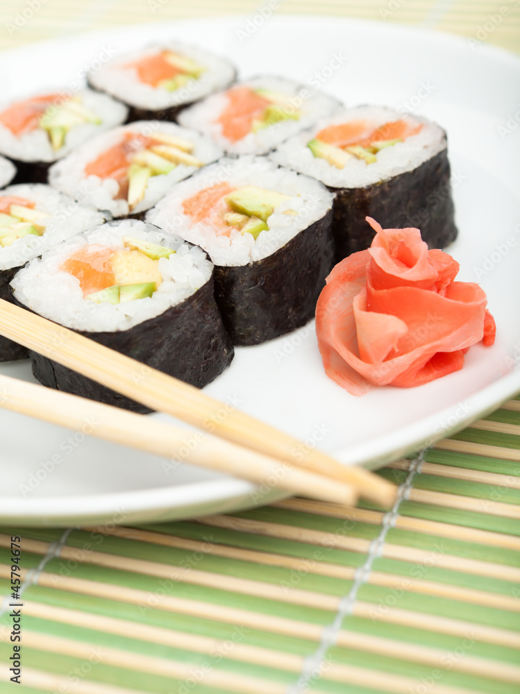 Sushi rolls on the plate with wood white chopsticks on green mat Sushi rolls on the plate with wood white chopsticks on green mat