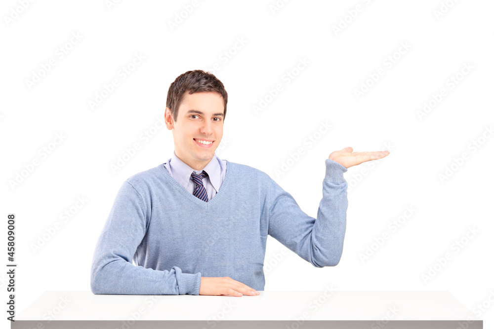 A smiling man sitting on a table and gesturing with his hand A smiling man sitting on a table and gesturing with his hand