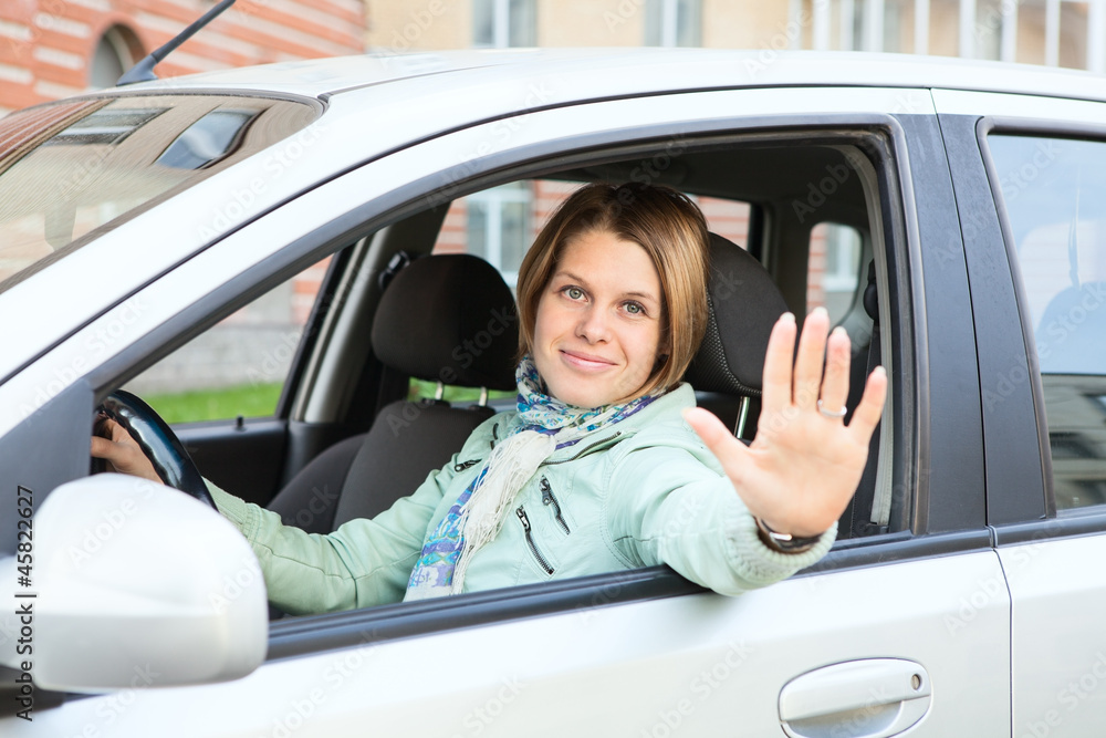 Blond hair greeting by hand and looking at camera from window