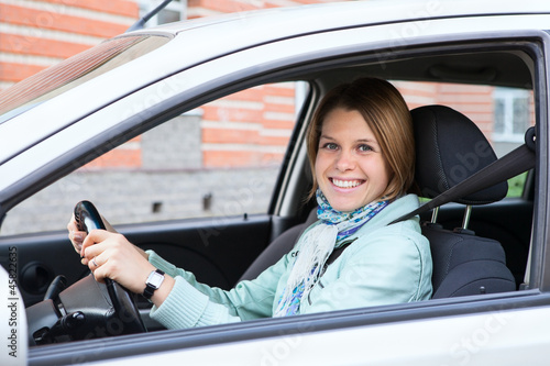 Happy blond woman holding steering wheel in new car © Kekyalyaynen