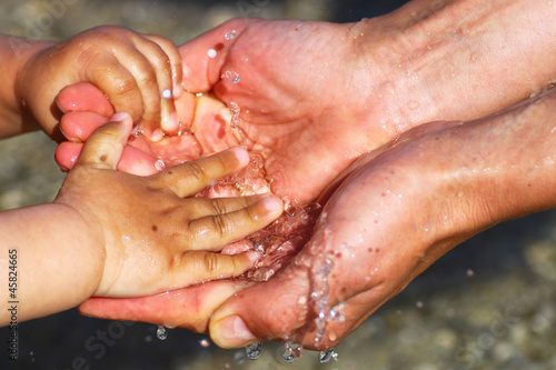 Hands of a baby and parent playing with water. Concept for parenthood, childhood and connectedness 