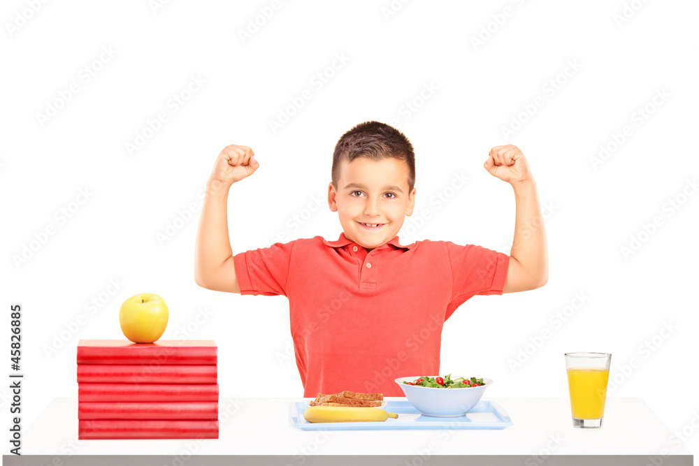 Strong boy showing his muscles and food on table during a breakf Strong boy showing his muscles and food on table during a breakf