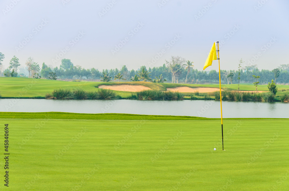 Obraz premium golf ball on green near hole with yellow flag
