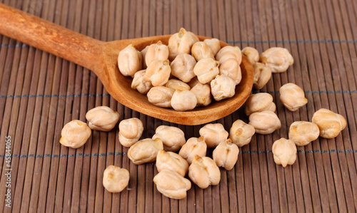 White chickpeas over wooden spoon on color background