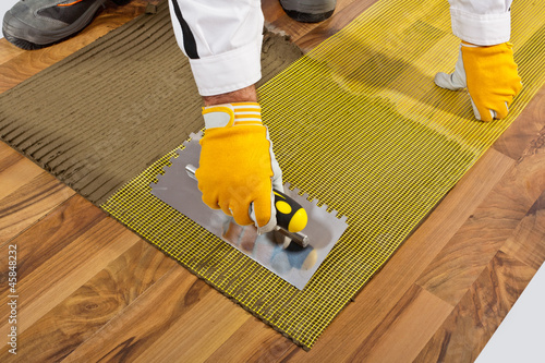 applies tile adhesive on wooden floor with reinforce fiber mesh