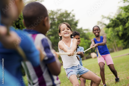Bild auf Leinwand Happy school children playing tug of war with rope in park