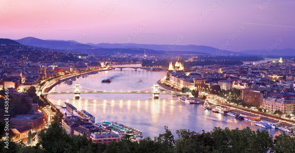 View of Budapest with Danube. Beautiful crimson sunset over Budapest. View of the evening city, houses, the parliament building. The sky is reflected in the river. Mountains in the background.
