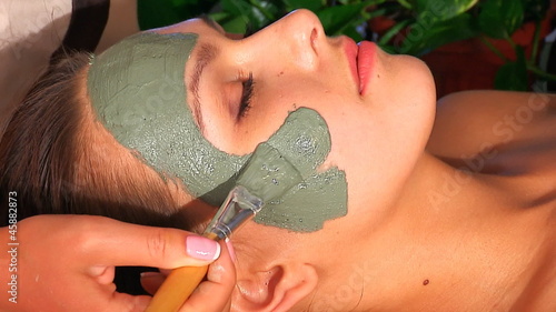 Woman with clay facial mask in beauty spa.